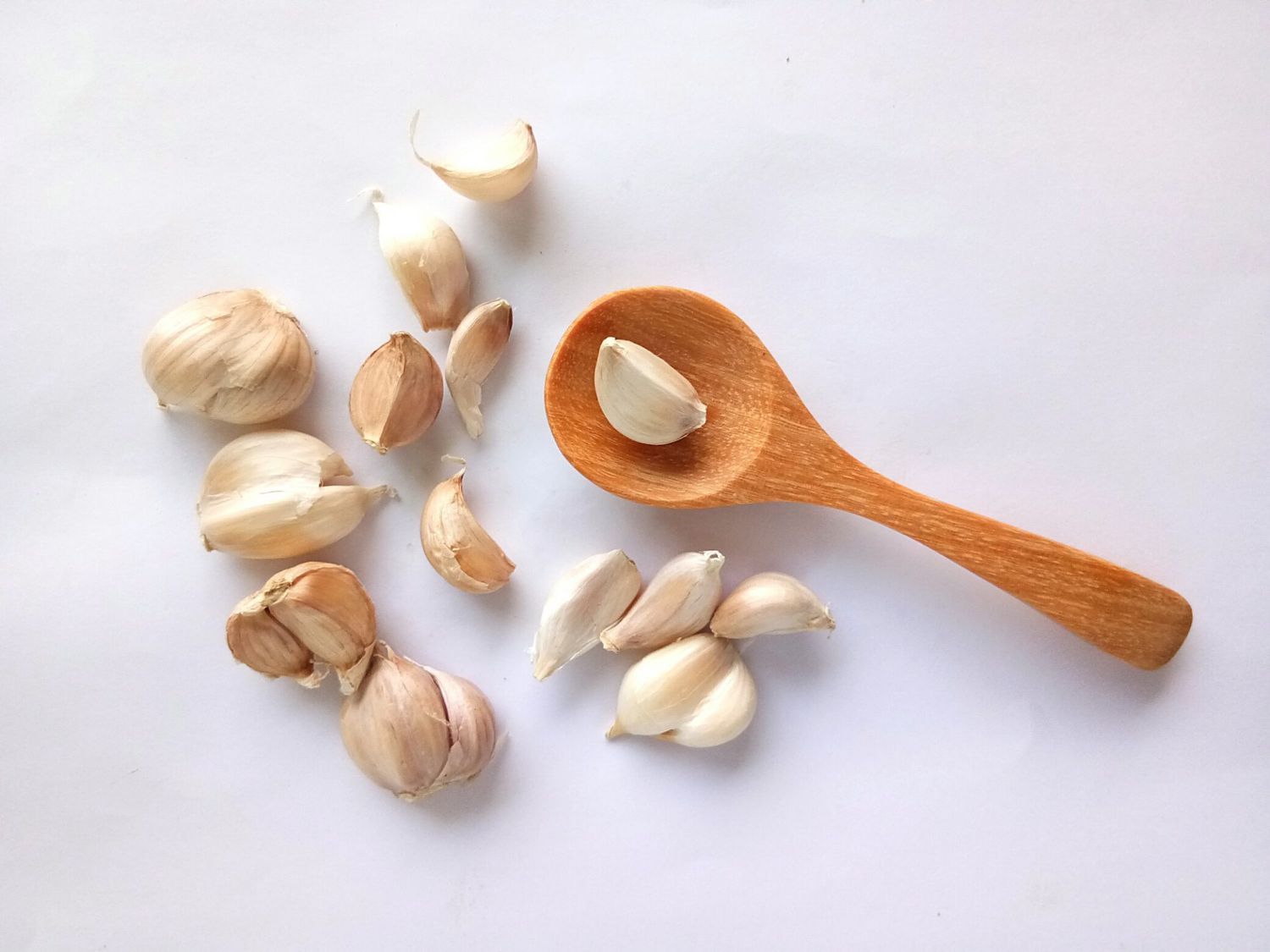 Raw white garlic bulbs and scattered cloves with a wooden spoon